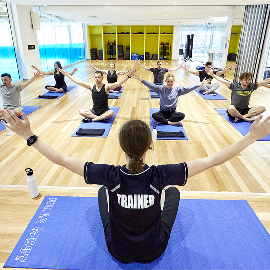 Group fitness class with female trainer leading a yoga pose